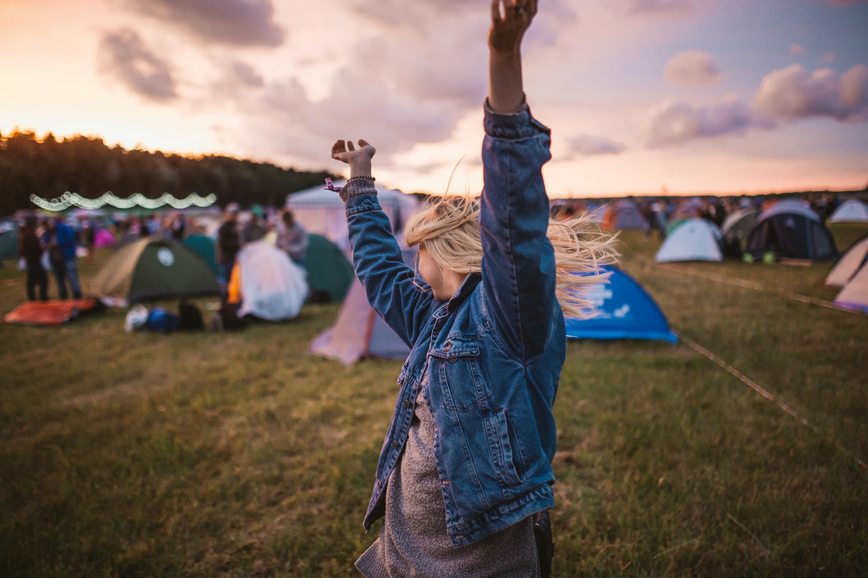 Asistente de festival con los brazos en alto frente a las tiendas de camping